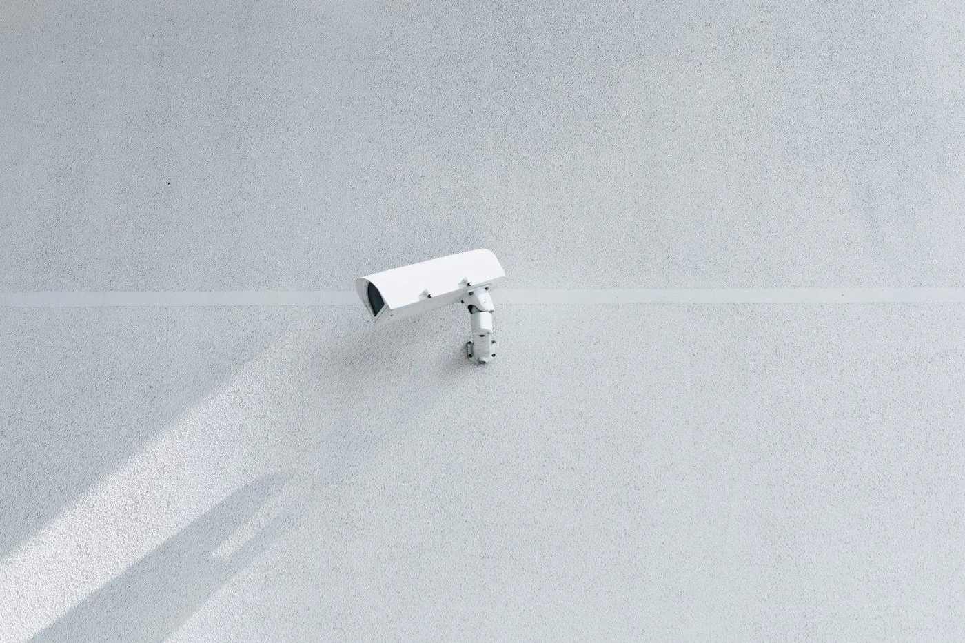 A white security camera on a pale rendered wall